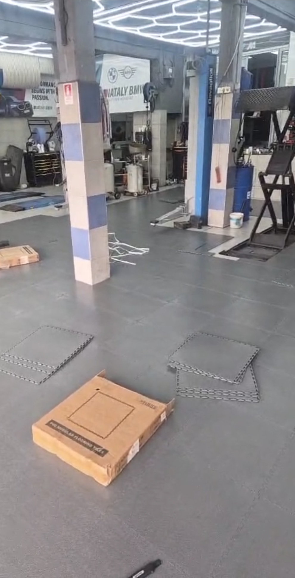 הנחת אריחי PVC אפורים באזור העבודה של מוסך, עם קרטון ואריחים לפני ההרכבה